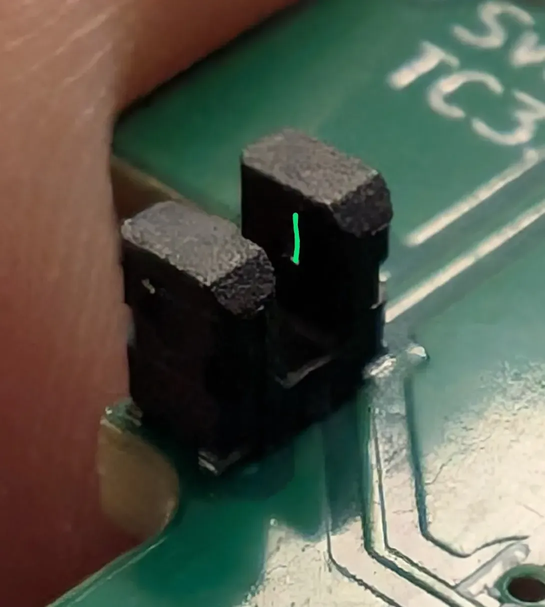 Close-up of a key sensor on the circuit board: a black block with a slot down the middle. A green mark shows one of the slits beside the slot.